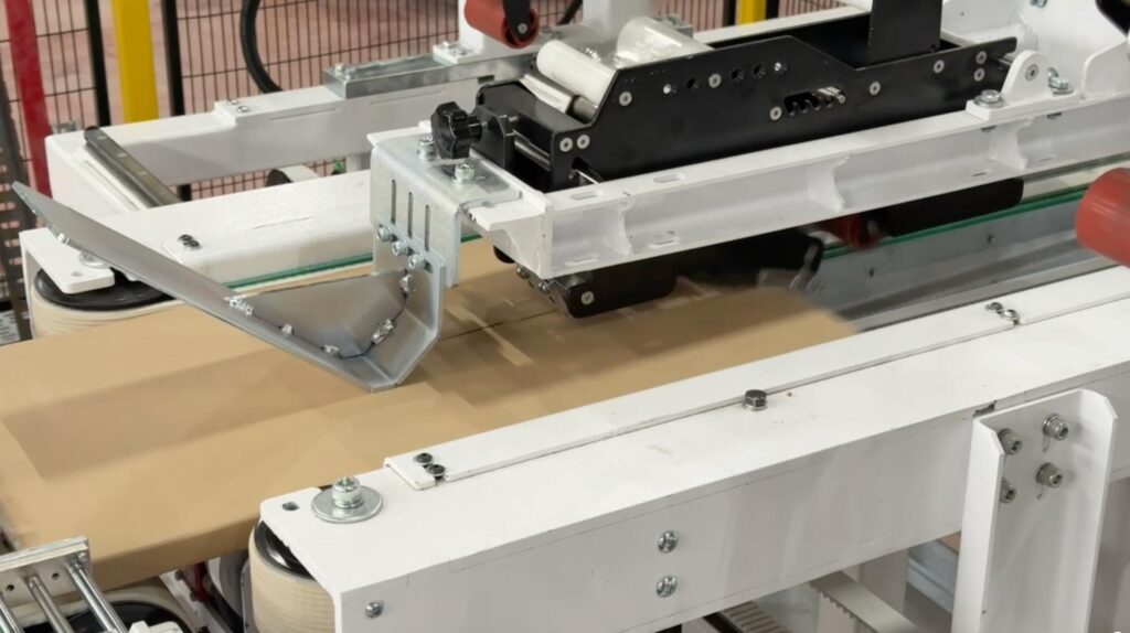 High-speed top-sealing and taping unit processing a flat-pack kit within the Edda Lotis automated packaging line.
